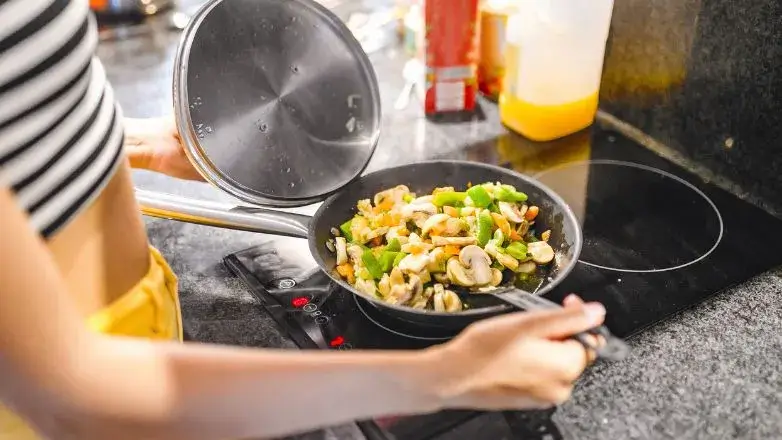 woman cooking food evenly in right cookware which is placed rightly over the induction stove